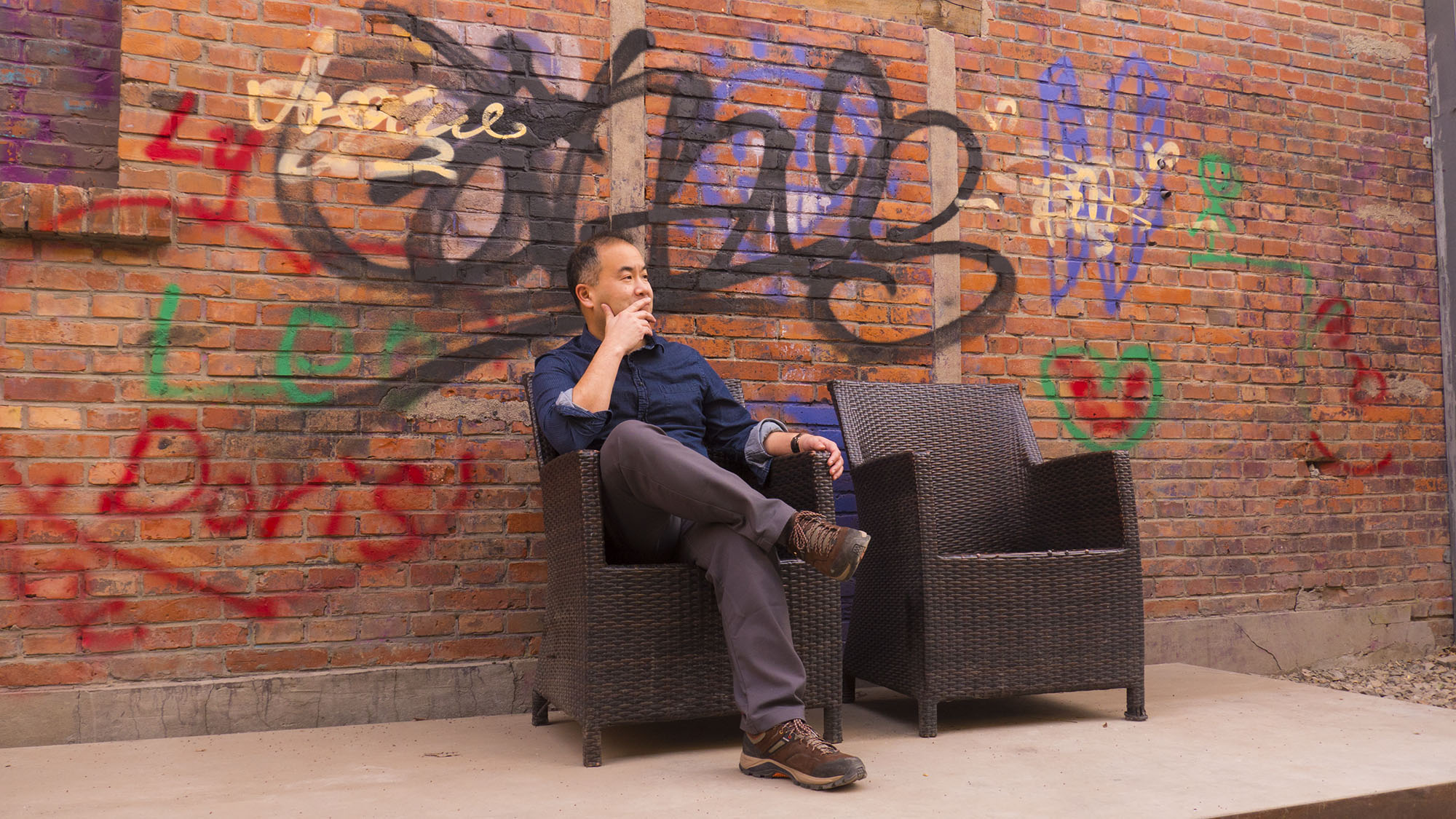 Ho Lin seated in front of a graffiti-covered brick wall in Beijing